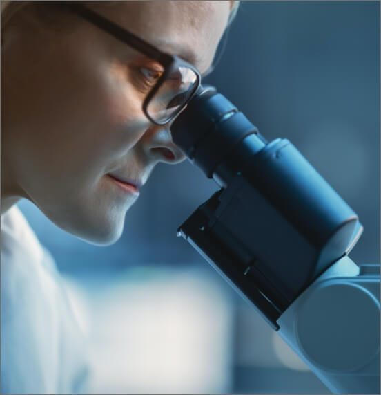 Person wearing glasses looking into a microscope.