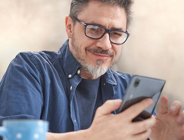 A man with a coffee mug smiles while scrolling on his iPhone